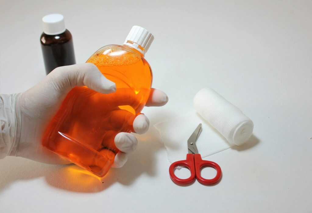 Hand holding orange antiseptic bottle with first aid items, ideal for healthcare themes.